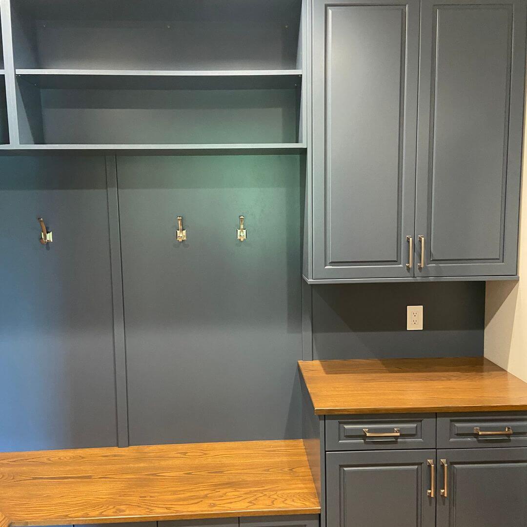 Blue-grey mudroom cabinetry with warm wooden benches and brass hardware